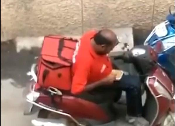 Muškarac sjedi na mopedu i jede hranu iz kutije za dostavu - Avaz