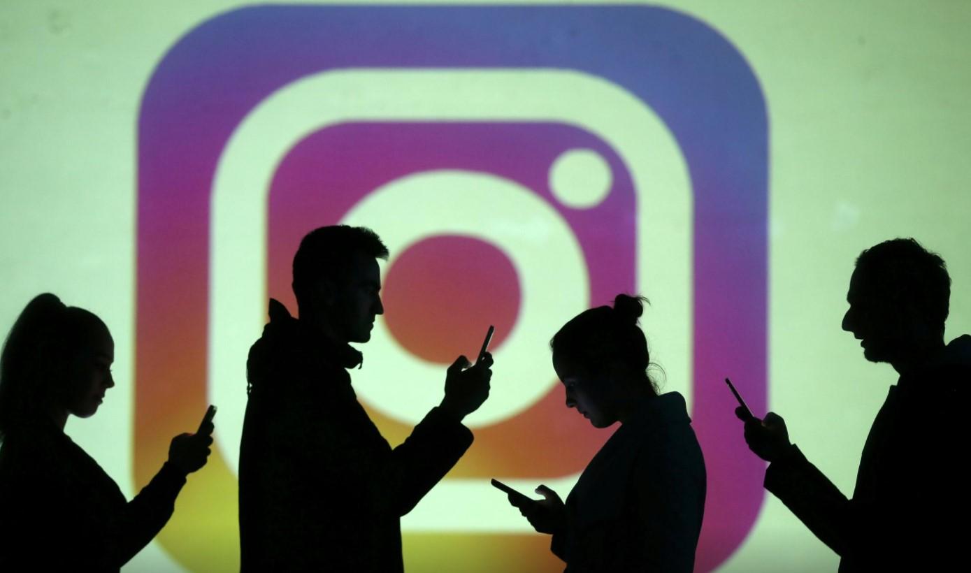 Silhouettes of mobile users are seen next to a screen projection of Instagram logo in this picture illustration taken March 28, 2018. - Avaz