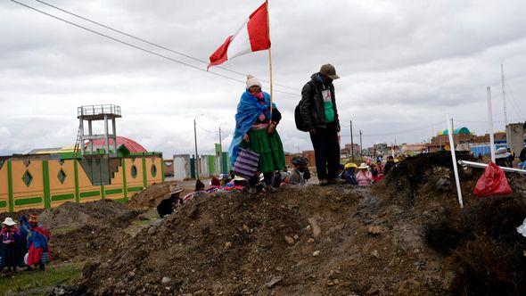 An Aymara woman, holding a Peruvian national, stands on a pile of dirt serving as a roadblock set up by anti-government protesters - Avaz