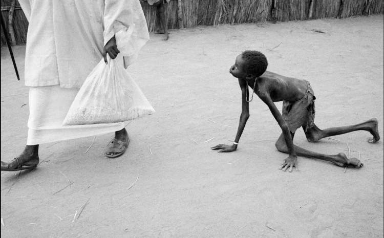 Sudan, 1998.: Dobro uhranjen muškarac krade kukuruz od izgladnjelog djeteta u centru za hranu Ljekari bez granica u Ajiepu. Glad je pogodila milione u Sudanu kasnih 1990-ih, pogoršana kršenjem ljudskih prava u sukobu između vladinih trupa i pobunjenika na jugu